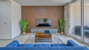 A modern living room with a flat-screen TV, a wooden coffee table, and blue sofas. - Beautiful, fully equipped 3BR in Sliema w/Balcony (Tas-Sliema)