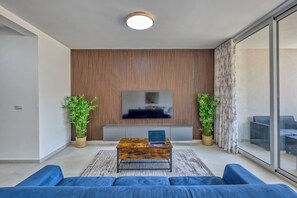 Ein modernes Wohnzimmer mit einem Flachbildfernseher, einem Holztisch und blauen Sofas.