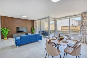 Ein modernes Wohnzimmer mit einem blauen Sofa, einem Esstisch für vier Personen und einem Fernseher, der an einer Holzwand angebracht ist.