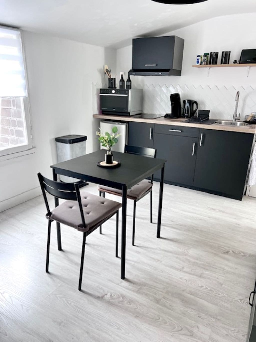 A modern kitchen with a dining table and chairs, a built-in oven, and a coffee machine.