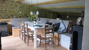A dining area with a stone wall, wooden beams, a table set with candles, and a television. - Holiday Home in Small Hamlet Surrounded by Fields and Mountains (Bouvières)