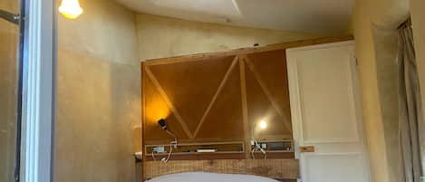 Een slaapkamer met een bed, nachtkastje, spiegel en raam.