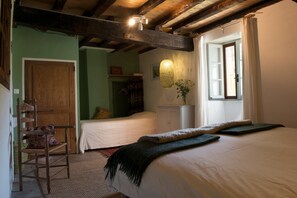 Una habitación con techo de madera, una cama con cubrecama blanco, una silla con cojín estampado y una mesita con un jarrón de flores.