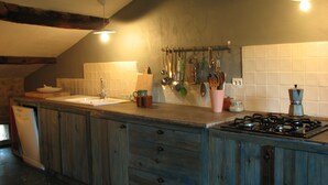 A kitchen with wooden cabinets, a gas stove, a sink, and various utensils hanging on the wall. - Holiday Home in Small Hamlet Surrounded by Fields and Mountains (Bouvières)