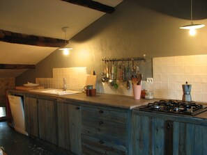 Eine Küche mit Holzschränken, einem Gasherd, einer Spüle und verschiedenen Küchenutensilien, die an der Wand hängen.