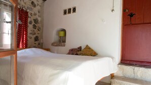 A bedroom with a bed, a stone wall, a red door, and a small window with a lamp. - Holiday Home in Small Hamlet Surrounded by Fields and Mountains (Bouvières)