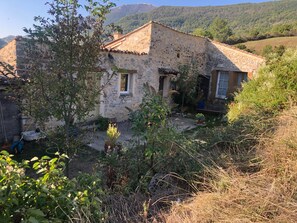 Una casa de piedra rústica con jardín delantero, rodeada de entorno natural.