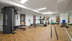 Ein Fitnessraum mit Trainingsgeräten, Holzboden und weißen Wänden.