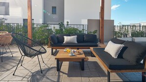 Eine Dachterrasse mit einem Holztisch, zwei schwarzen Sofas und einem schwarzen Sessel.