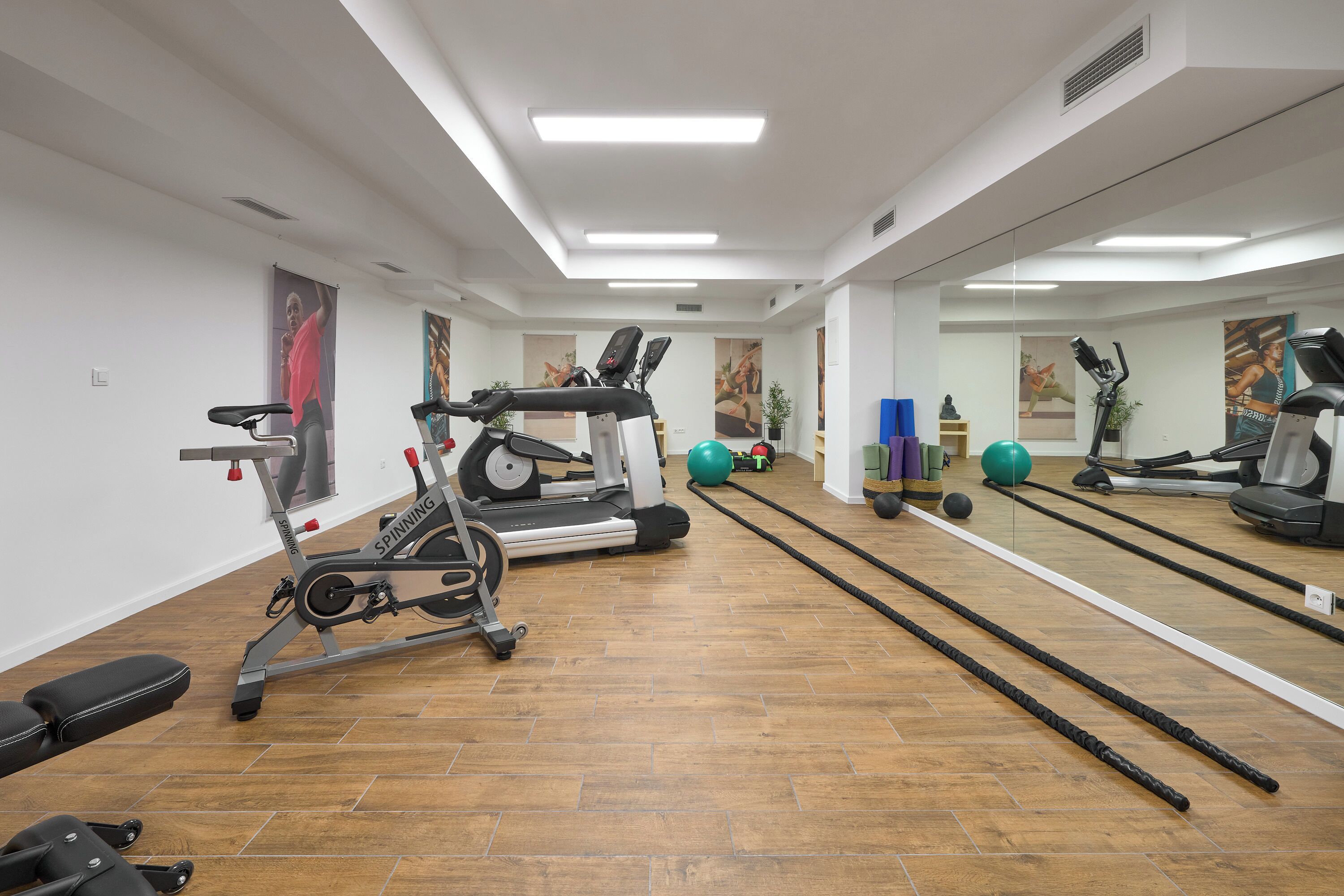 A gym with exercise equipment, a mirrored wall, and wooden flooring.