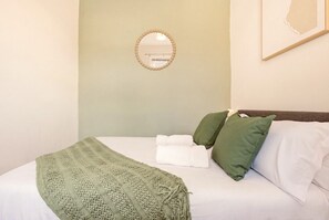Ein Bett mit einer grünen Strickdecke, weißen Kissen und einem runden Spiegel an der Wand.