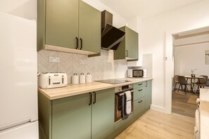 A modern kitchen with a built-in oven, microwave, and toaster. There is a dining area with a table and chairs visible in the background. - The Sandringham - North East Escapes (Sunderland)