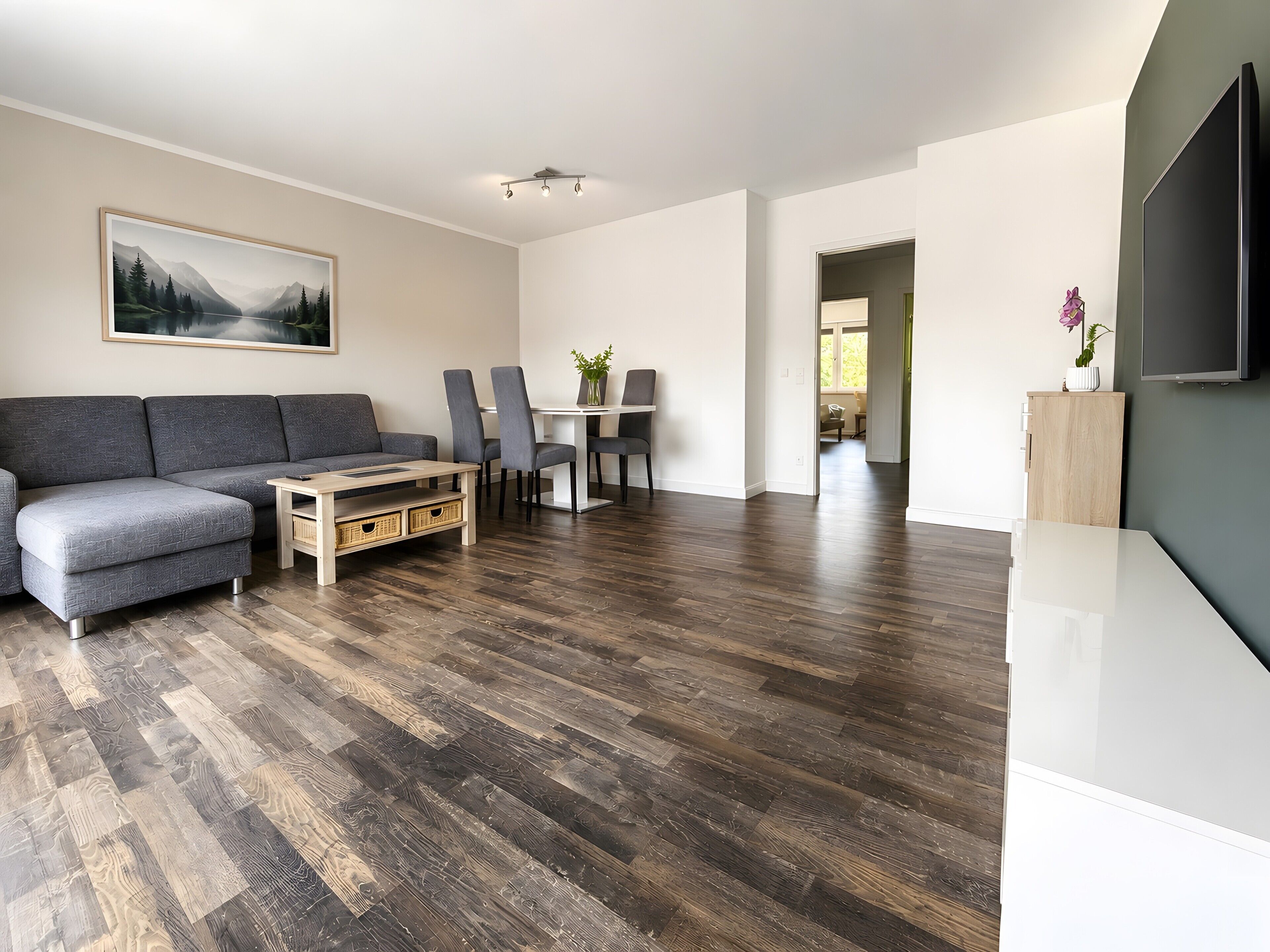 Ein modernes Wohnzimmer mit einer Eckcouch, einem Esstisch mit Stühlen und einem an der Wand befestigten Flachbildfernseher.