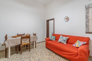 Une pièce comprenant une table à manger et des chaises, un canapé avec des coussins à motifs et une horloge murale.