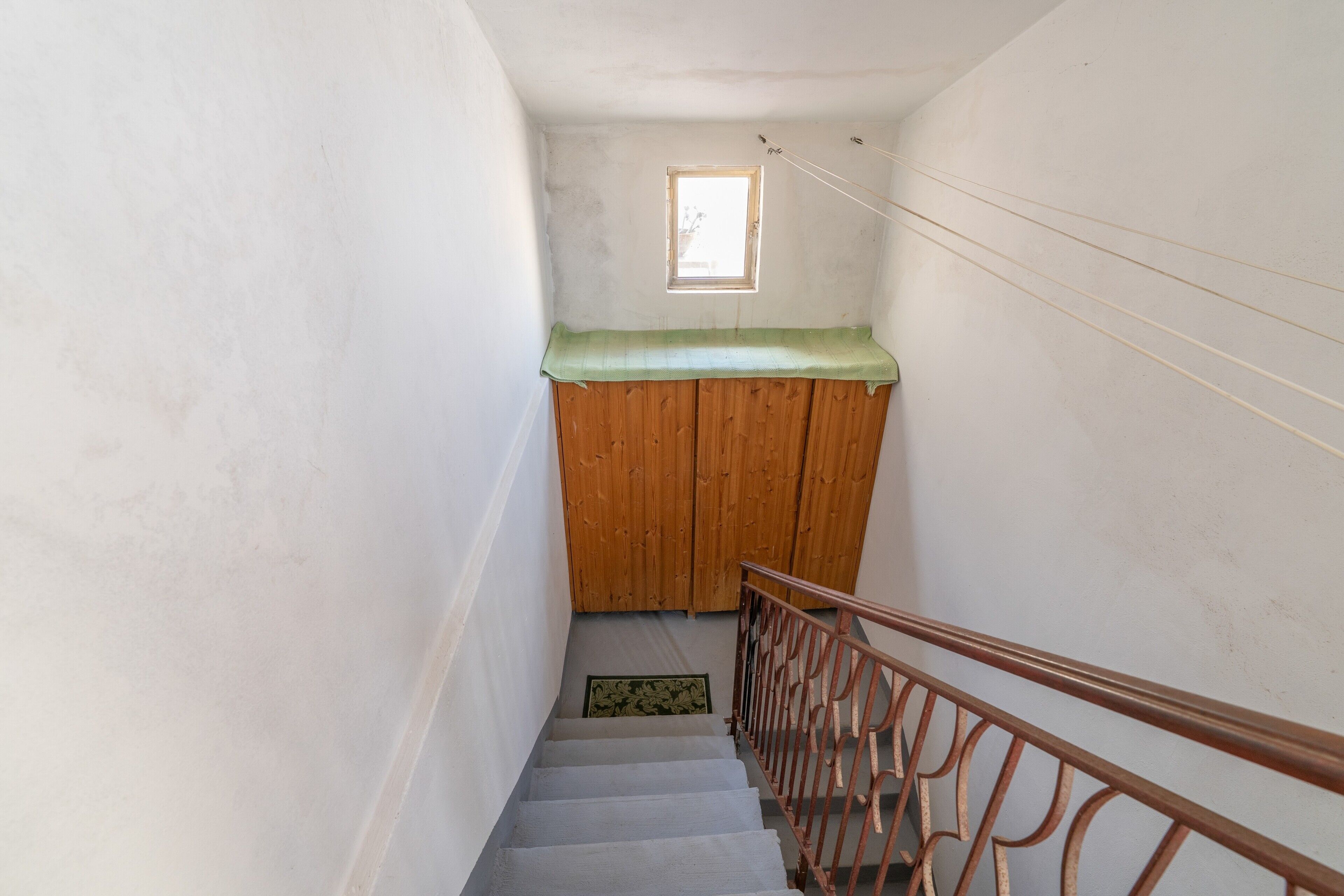 Eine schmale Treppe mit hölzernem Handlauf und einem kleinen Fenster am obersten Ende.