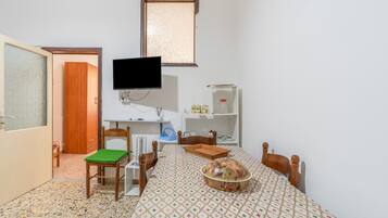 Une pièce comprenant une table à manger, des chaises, un téléviseur et une fenêtre.