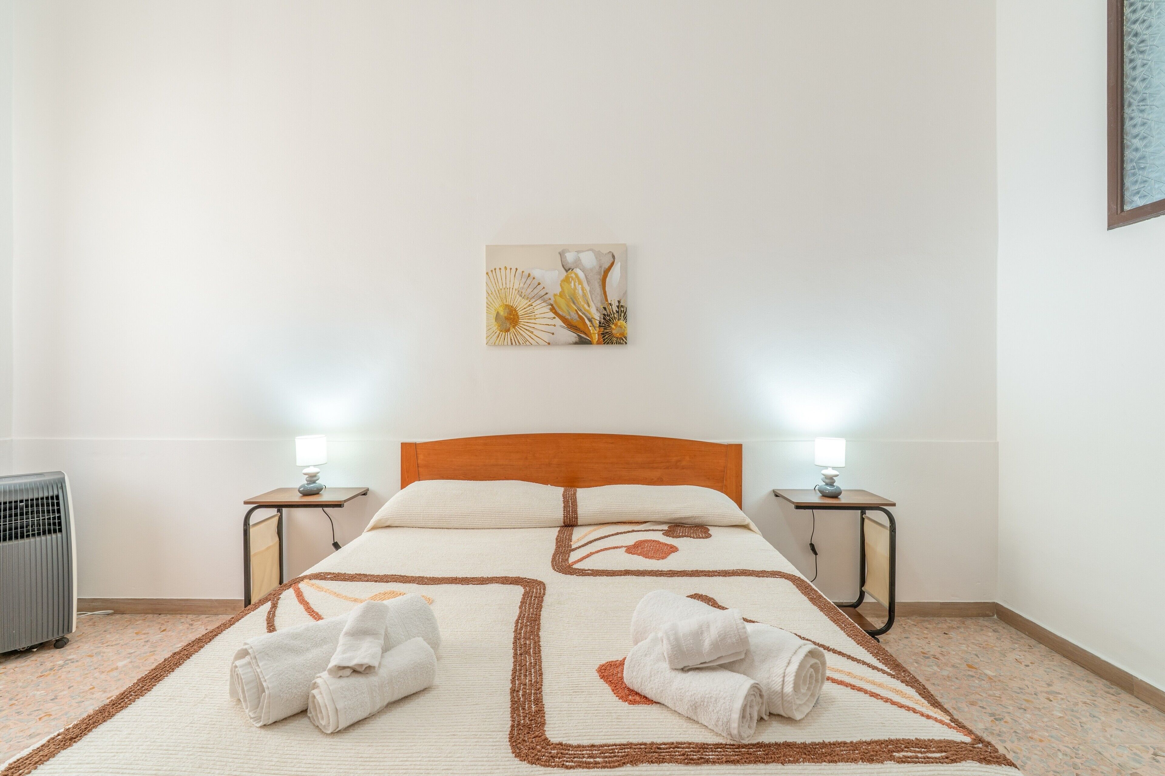Une chambre d’hôtel avec un lit, deux lampes de chevet, un radiateur et un tableau au mur.
