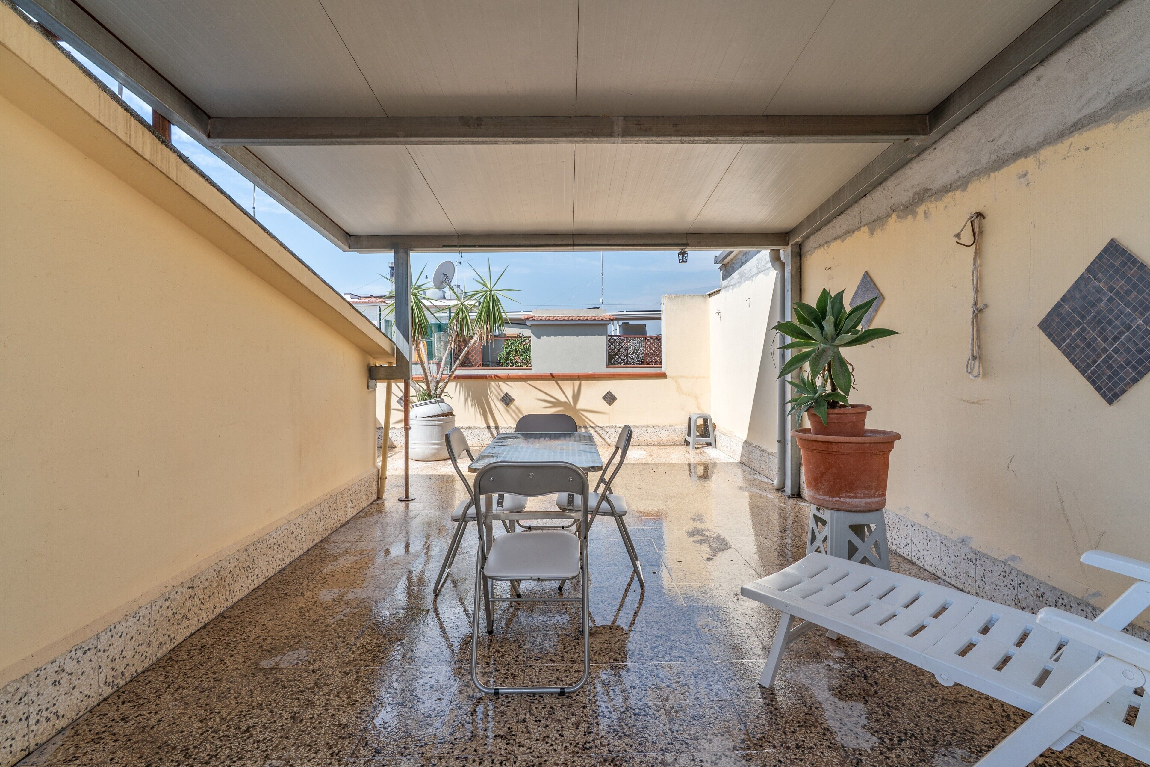 Une terrasse extérieure couverte, avec une table et des chaises, des plantes en pot et un banc blanc.