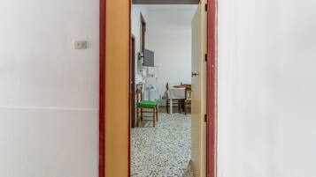 Un passage mène à une pièce dont le sol est recouvert de carreaux, et qui contient une chaise, une table et un téléviseur fixé au mur.