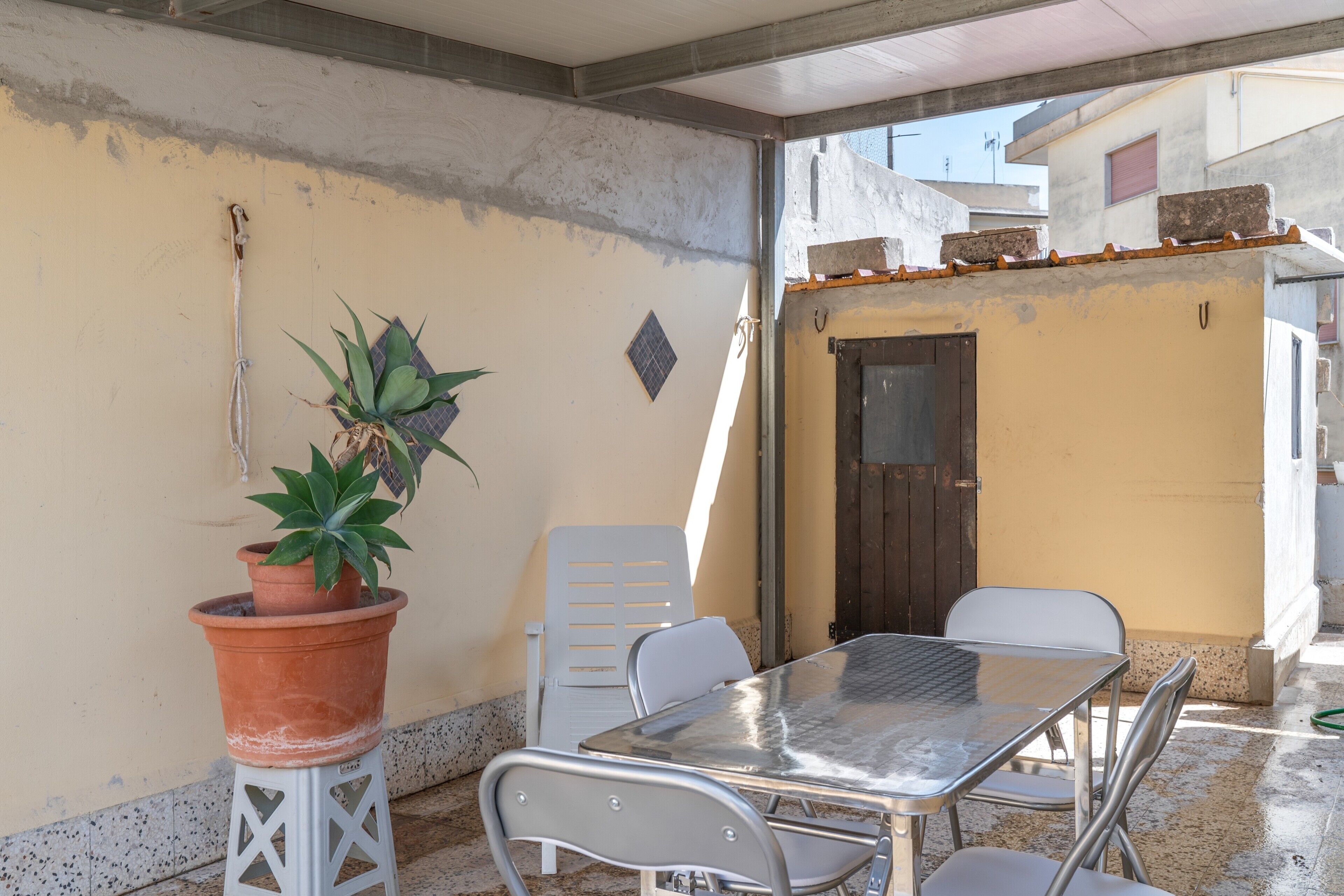 Eine Terrasse mit einem Metalltisch und -stühlen, einem Blumentopf und einer kleinen Tür.