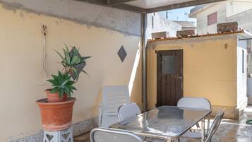 Un espace patio avec une table et des chaises en métal, une plante en pot et une petite porte.