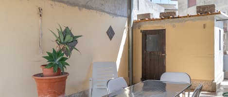 A patio area with a metal table and chairs, a potted plant, and a small door.