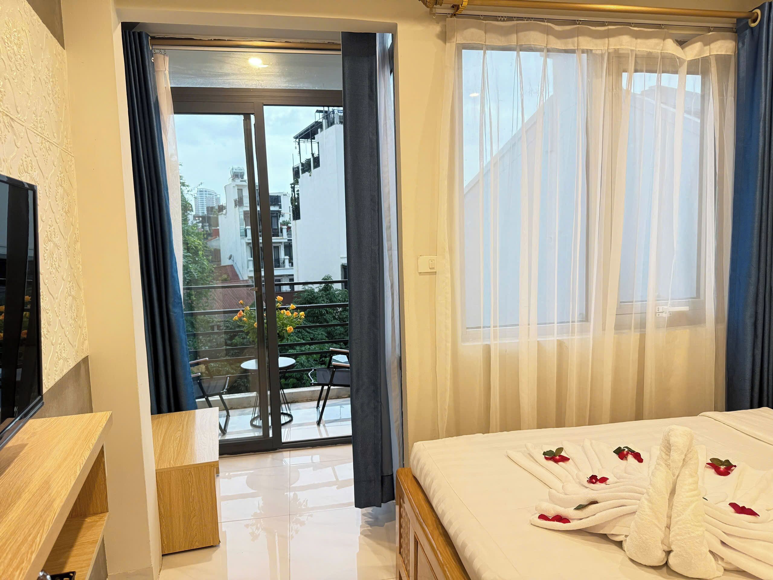 Quarto de hotel com uma cama, uma secretária de madeira, uma porta de correr de vidro para uma varanda e vista para a paisagem urbana.
