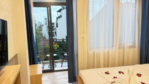 A hotel room with a bed, a wooden desk, a sliding glass door to an outdoor balcony, and a view of the cityscape. - Silver Lantern Hanoi Hotel (Hanoi)