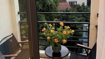 A balcony with a table and chairs, a vase with flowers, and a view of buildings and trees.