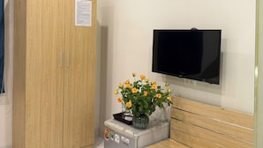 A room with a wooden wardrobe, a small refrigerator, a bench, a television mounted on the wall, and a pair of shoes on the floor. - Silver Lantern Hanoi Hotel (Hanoi)