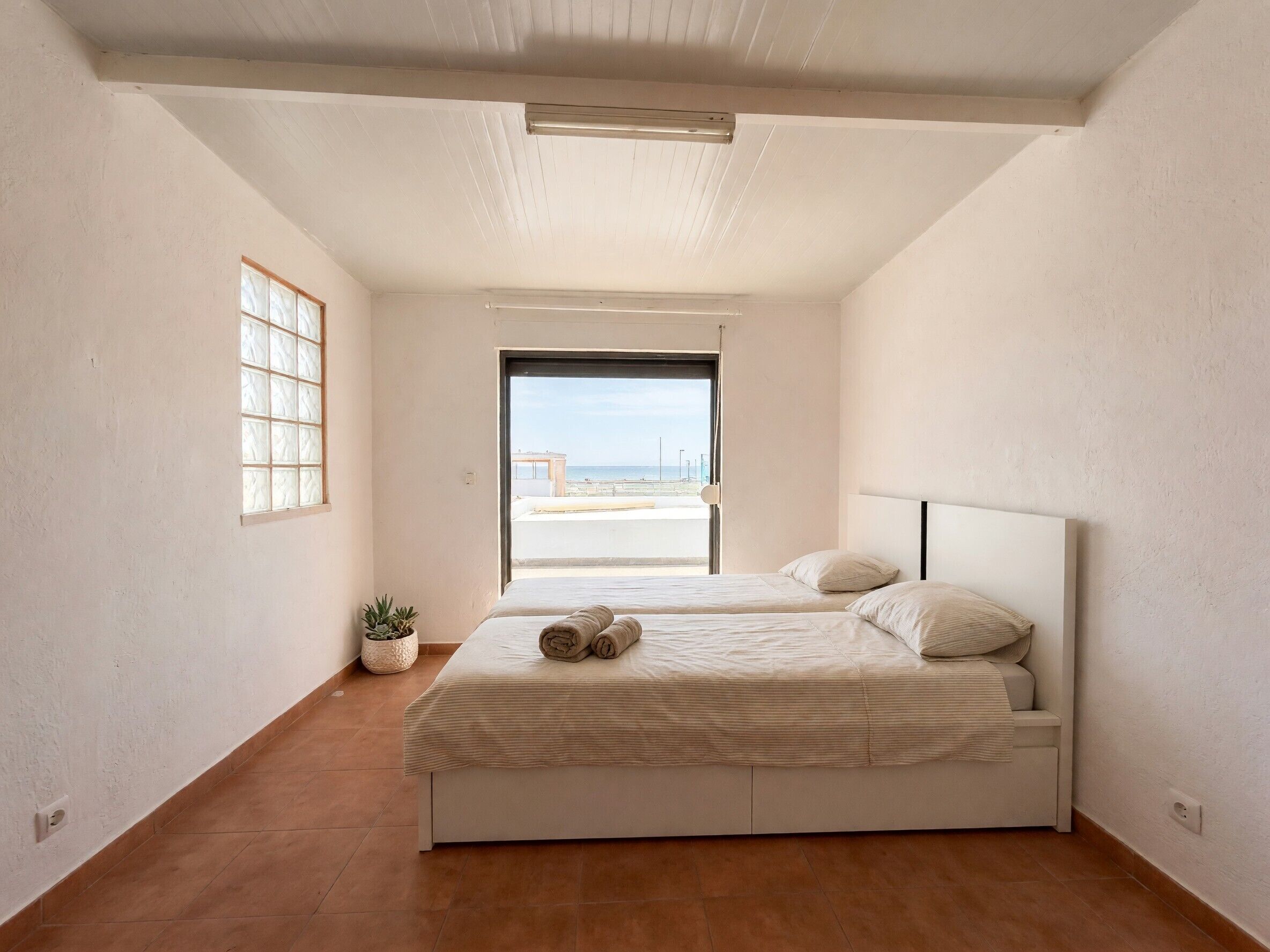 Une chambre à coucher avec un lit, une plante en pot et une vue sur la mer.