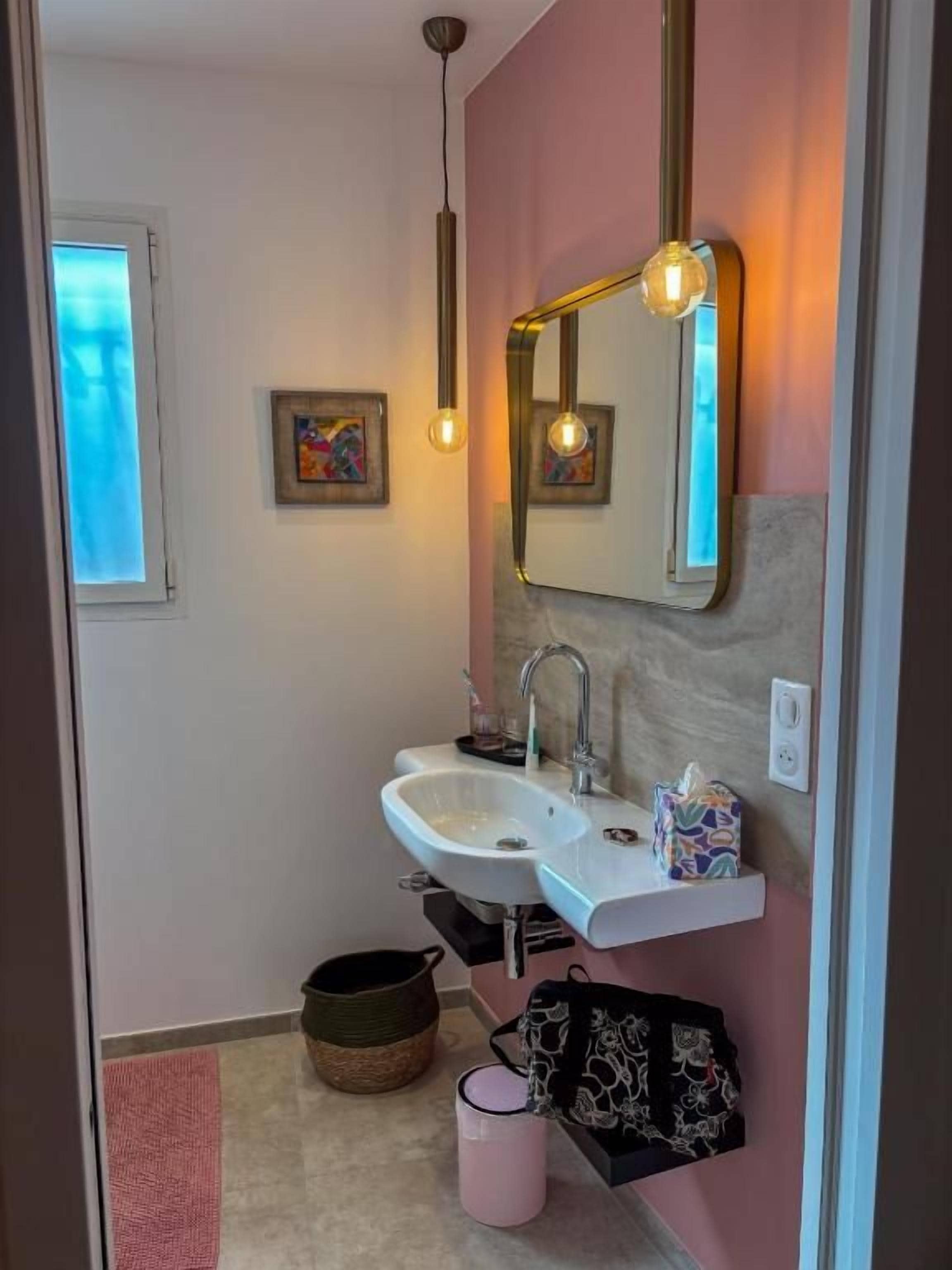 A bathroom with a white sink, a mirror, and a hanging light fixture.
