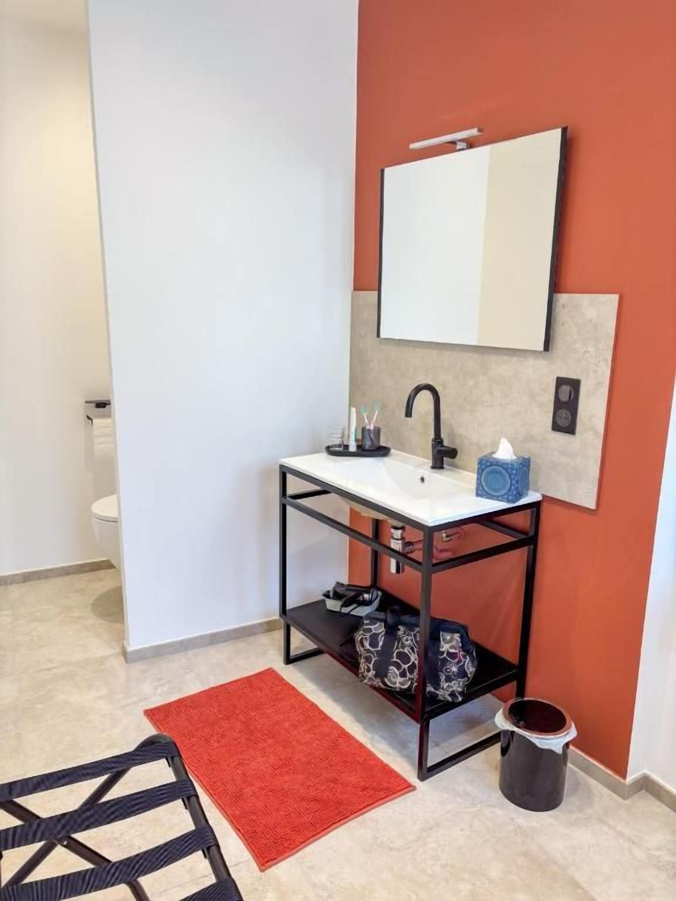Ein Badezimmer mit einem weißen Waschbecken, einem schwarzen Metallgestell, einem roten Teppich und einer weißen Wand.