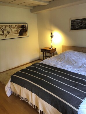 Een slaapkamer met een bed, een nachtkastje met een lamp, een schilderij aan de muur en een vloerkleed.