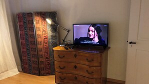 Television on puukehikkoisella lipastolla, taustalla kuvioitu seinävaate.