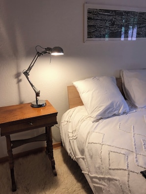 A bedroom with a wooden nightstand, a desk lamp, a bed with white bedding, and a framed picture on the wall. - The historic town of Laupen near Bern—Top-Notch Apartment on the 1st Floor (Laupen)
