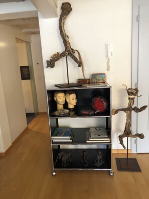 A room with a wooden sculpture on the wall, a bookshelf with books and decorative items, and a door with a light switch. - The historic town of Laupen near Bern—Top-Notch Apartment on the 1st Floor (Laupen)