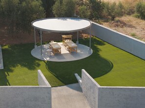 A circular outdoor seating area with tables and benches, surrounded by a concrete wall and green artificial grass. - Ariselia Villa, Grand Spaces, Wellness & Play (Retymno)