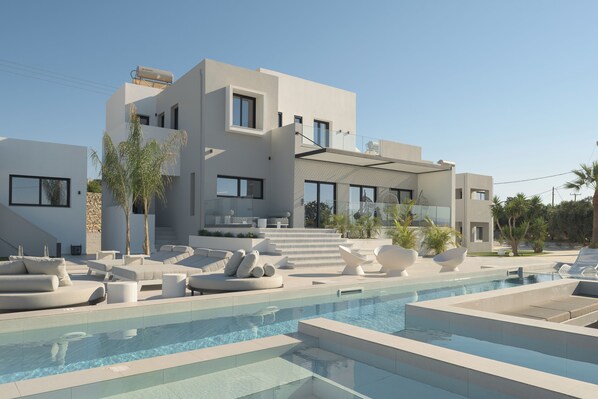 Une maison moderne à plusieurs étages, dotée d’une piscine, d’un espace de détente extérieur et d’un escalier menant aux niveaux supérieurs.