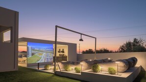 A modern outdoor seating area with a large screen displaying a scenic landscape, surrounded by well-lit plants and a contemporary design. - Ariselia Villa, Grand Spaces, Wellness & Play (Retymno)