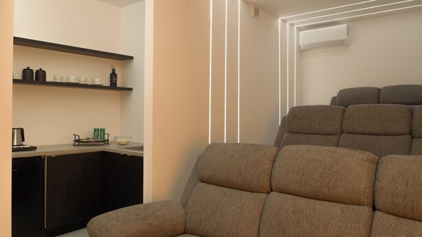 A modern living room with a sofa and a kitchen area with shelves. - Ariselia Villa, Grand Spaces, Wellness & Play (Retymno)