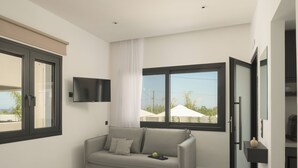 A modern bedroom with a grey sofa, a flat-screen TV mounted on the wall, and a large window offering a view of the outdoors. - Ariselia Villa, Grand Spaces, Wellness & Play (Retymno)