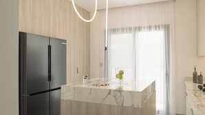 A modern kitchen with a marble island, a black refrigerator, and a window with sheer curtains. - Ariselia Villa, Grand Spaces, Wellness & Play (Retymno)