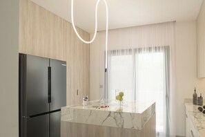Eine moderne Küche mit einer Marmor-Kochinsel, einem schwarzen Kühlschrank und einem Fenster mit durchsichtigen Vorhängen.