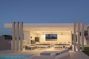 Un espace de vie extérieur moderne, doté d’une piscine, d’un coin salon et offrant une vue sur le paysage environnant.