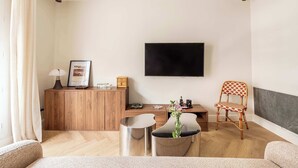 A modern living room with a wooden cabinet, a small round table, a chair, and a television mounted on the wall. - 1BR with Eiffel Tower View - Near Arc de Triomphe (Paris)