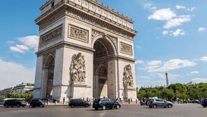 A large, historic stone arch monument with intricate carvings and inscriptions, surrounded by a busy street with cars and pedestrians. - 1BR with Eiffel Tower View - Near Arc de Triomphe (Paris)