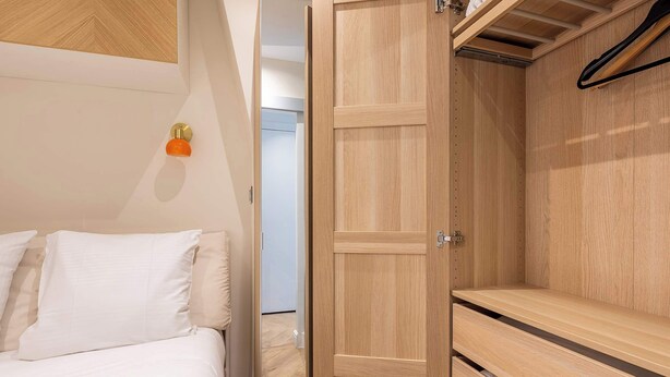 A hotel room with a bed, a wooden wardrobe, and a wall-mounted towel rack. - 1BR with Eiffel Tower View - Near Arc de Triomphe (Paris)