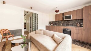 A modern living room with a beige sofa, a glass coffee table, and a wicker chair. - 1BR with Eiffel Tower View - Near Arc de Triomphe (Paris)