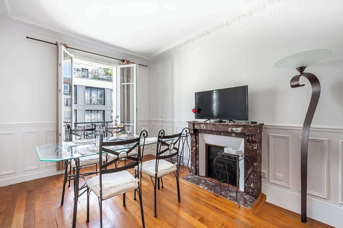 A dining area with a glass table and chairs, a fireplace, and a television on a stand.
